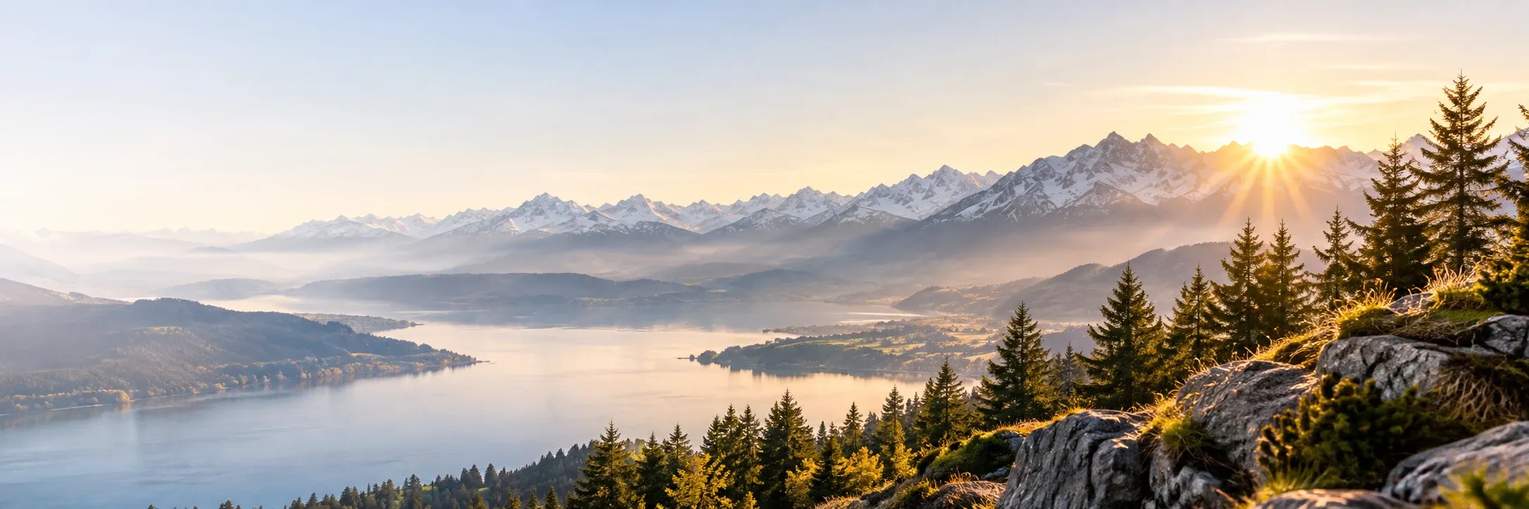 An alpine lake at sunrise with snowy peaks and fir trees.