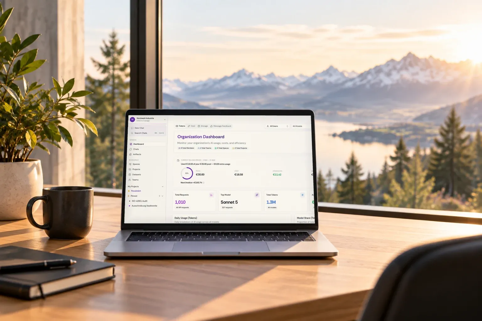 A laptop on an oak desk by a window over an alpine lake, showing the oneAI organisation dashboard.